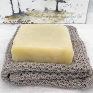 a solid soap bar sat on a handmade linen face cloth. the solid soap bar is called fresh facial bar and is handmade in Scotland by Made in the Glen. It is a natural soap and a lovely creamy colour. The linen face cloth is an oatmeal colour