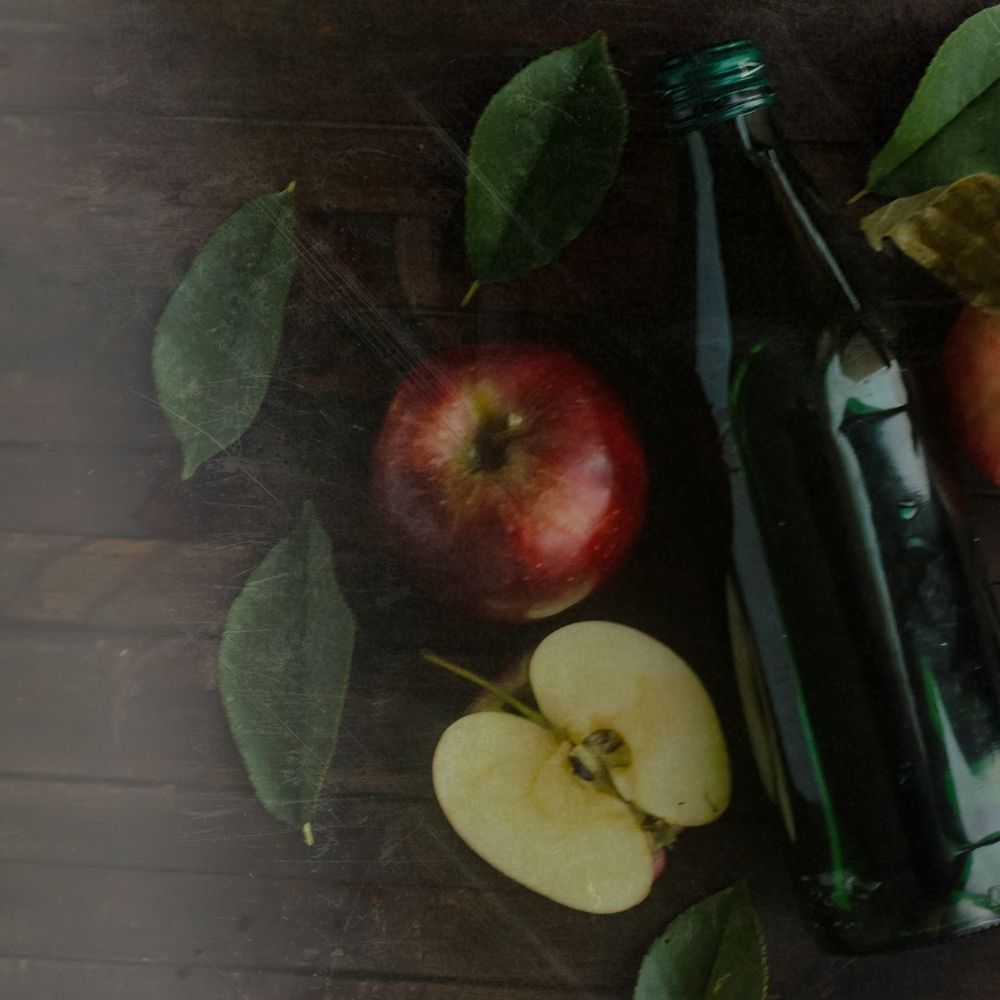 some apples, one is cut open, are ladi on a dark table with a bottle of apple cider vinegar next to in ready to make an ACV hair rinse