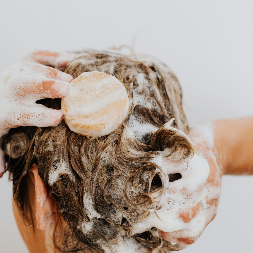 A picture of a lady washing her hair with a solid shampoo bar.
