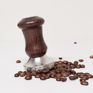 Wenge Coffee Tamper handmade in Scotland frm Wenge wood, stainless steel tamper and a wenge handle, the tamper is photographed on a white background and is slightly tilted with coffee beans underneath it and round it