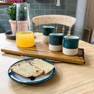 Handcrafted whisky stave chopping board on a wooden table, styled with a jug and part glazed blue beakers, highlighting the rich wood grain and artisanal craftsmanship