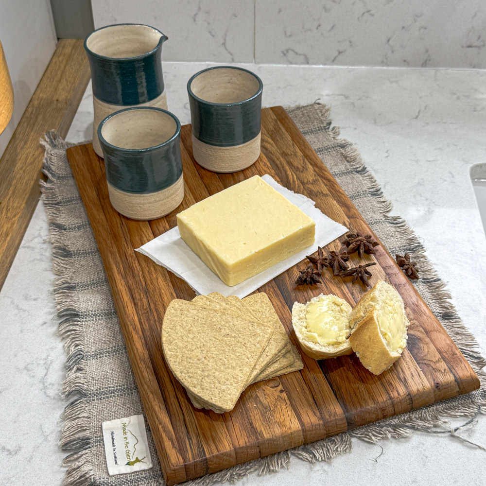 oak chopping board with rich grain detail, styled against green Fired Earth tiles, while marble and a vintage jug.
