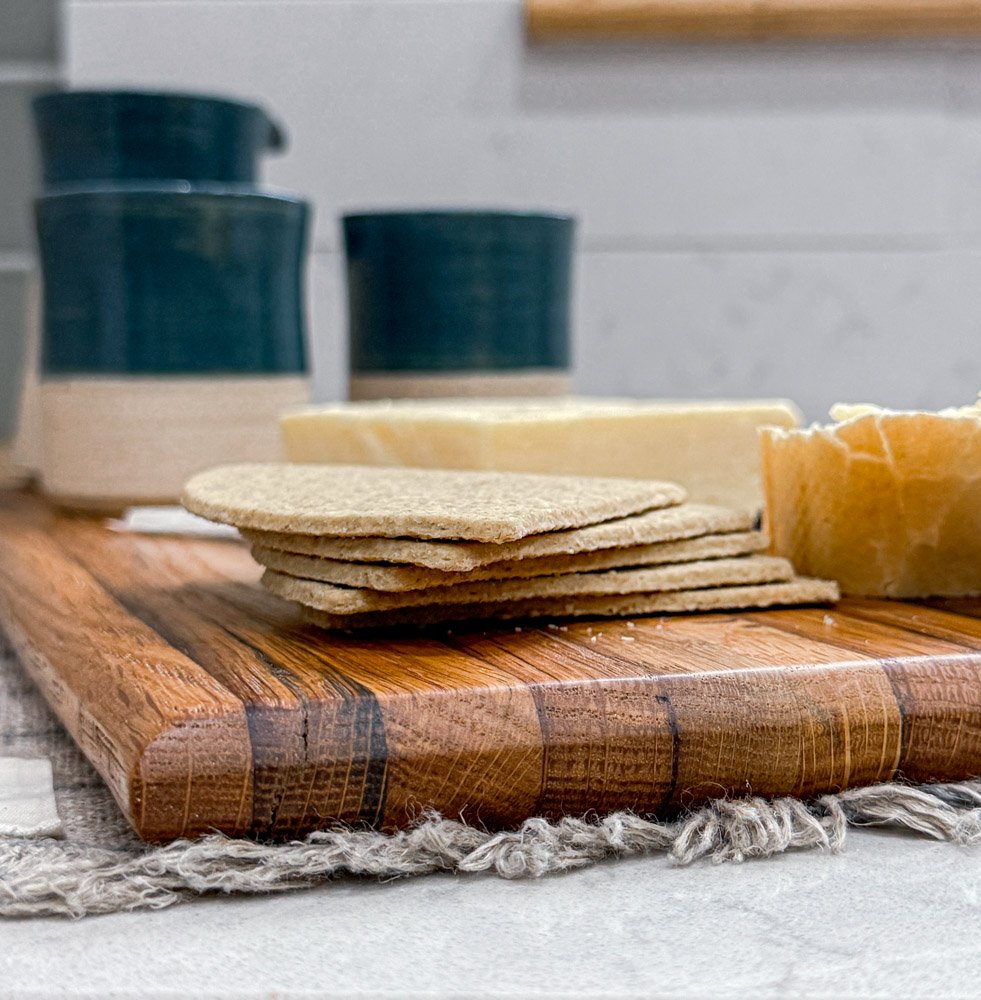 oak chopping board with rich grain detail, styled against green Fired Earth tiles, while marble and a vintage jug.