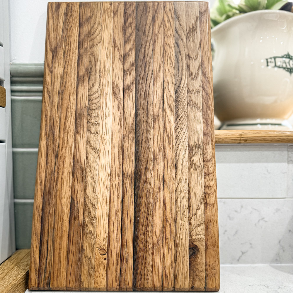 oak chopping board with rich grain detail, styled against green Fired Earth tiles, while marble and a vintage jug.
