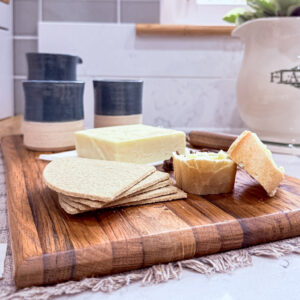 oak chopping board with rich grain detail, styled against green Fired Earth tiles, while marble and a vintage jug.