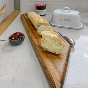 whisky cask grazing or garlic bread board for tearing and sharing with a baguette on it with a pot of bonne maman jam behind and an enamal white butter dish set on white marble kitchen worktop. the grazing board is made from whisky staves and is handmade in Scotland
