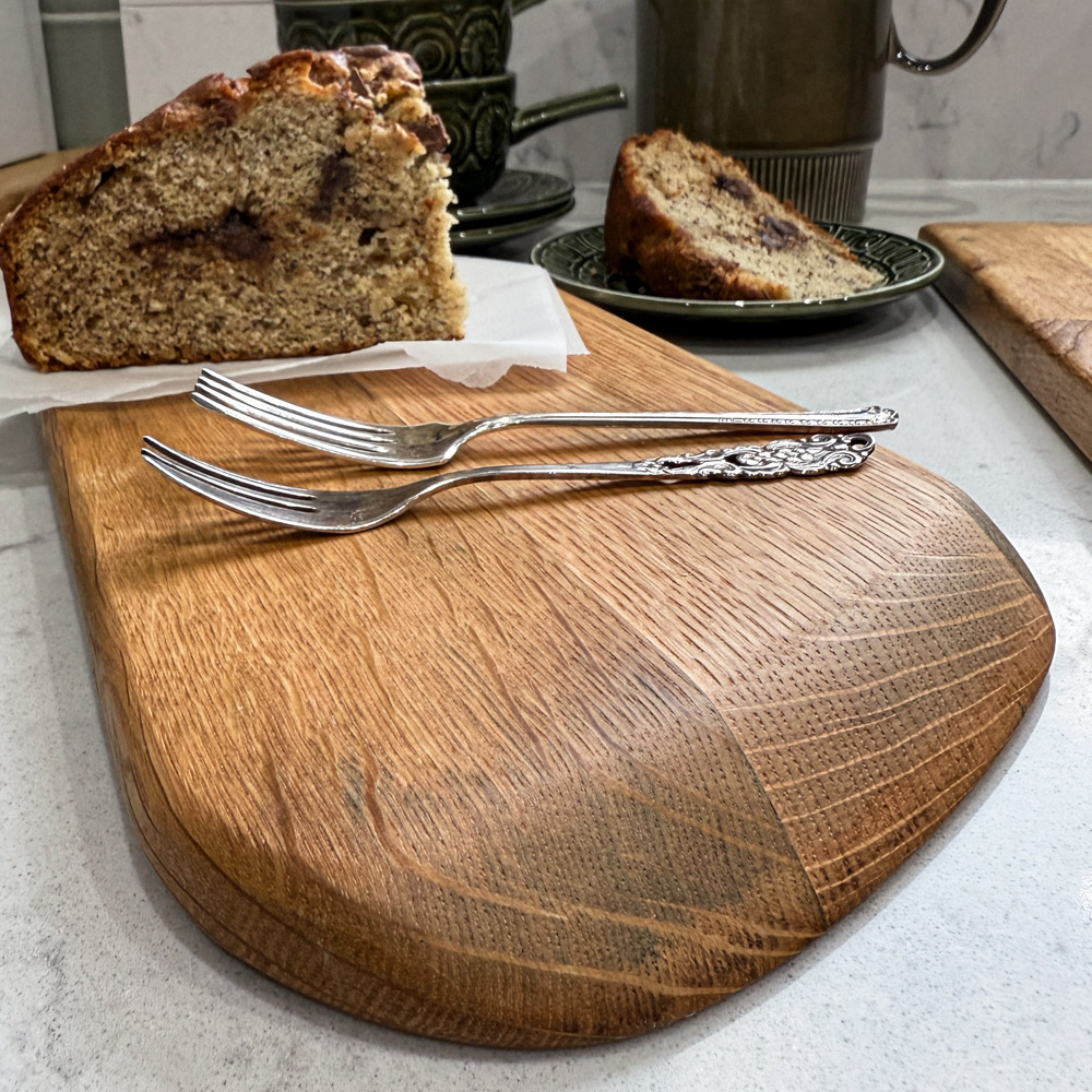 reclaimed oak whisky lid paddle board with unique handle, displaying a slice of banana cake on a napkin, and vintage crockery nearby