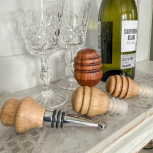 Made in the Glen's Handmade in Scotland Bottle Stopper Collection laid on a shelf with some wine glasses and an open bottle of wine the bottle stoppers are handmade from local and reclaimed wood