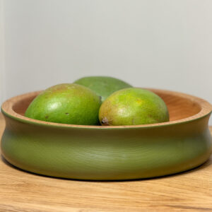 Restored Oak Bowl painted in coats olive green paint place on an oak table with three limes inside the bowl