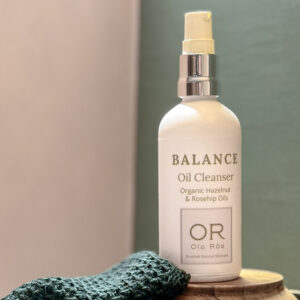 balance oil cleanser in white matte glass bottle against green and pink background. handmade in Scotland with natural and organic oils