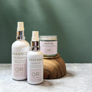 the complete ritual set out on a grey worktop a white bottle of balance oil cleanser, a white bottle of restore facial oil and a jar of refine purifying facial masque