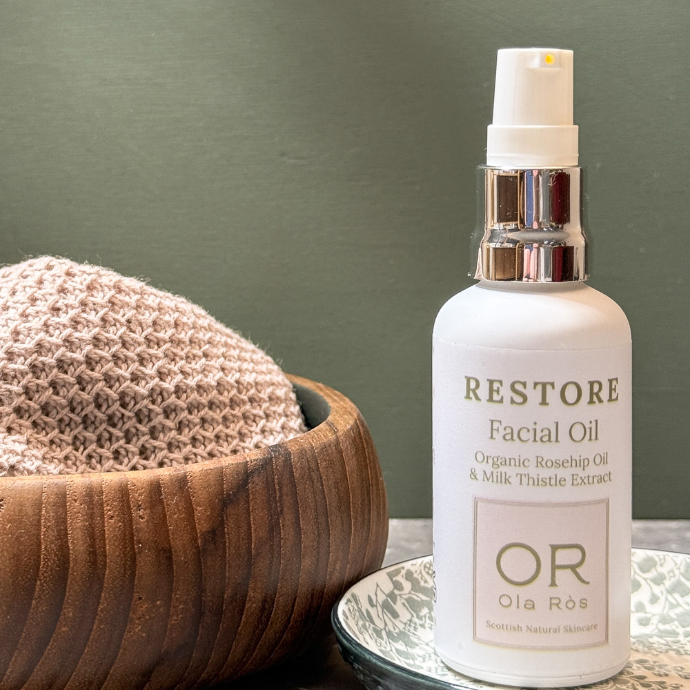 Restore facial oil by ola rs skincare skincare made in scotland the bottle of restore facial oil is stood on a plate with a wooden bowl and a pink handmade face cloth beside it