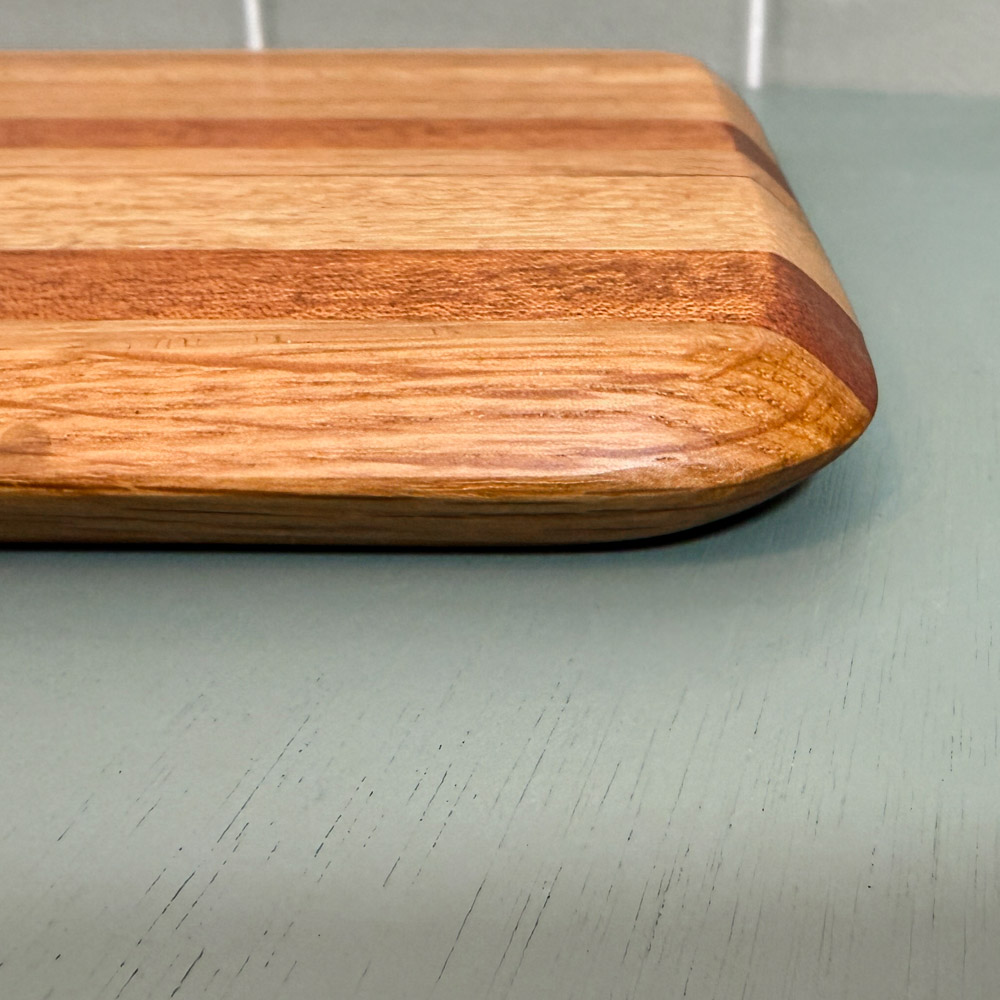 subtly striped handmade oak and mahogany chopping board made from oak and mahogany laying on a green table
