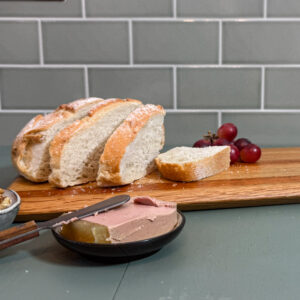 subtly striped handmade oak and mahogany chopping board made from oak and mahogany laying on a green table styled with bread grapes and pate with a green tiled background the board was handmade in scotland from reclaimed materials