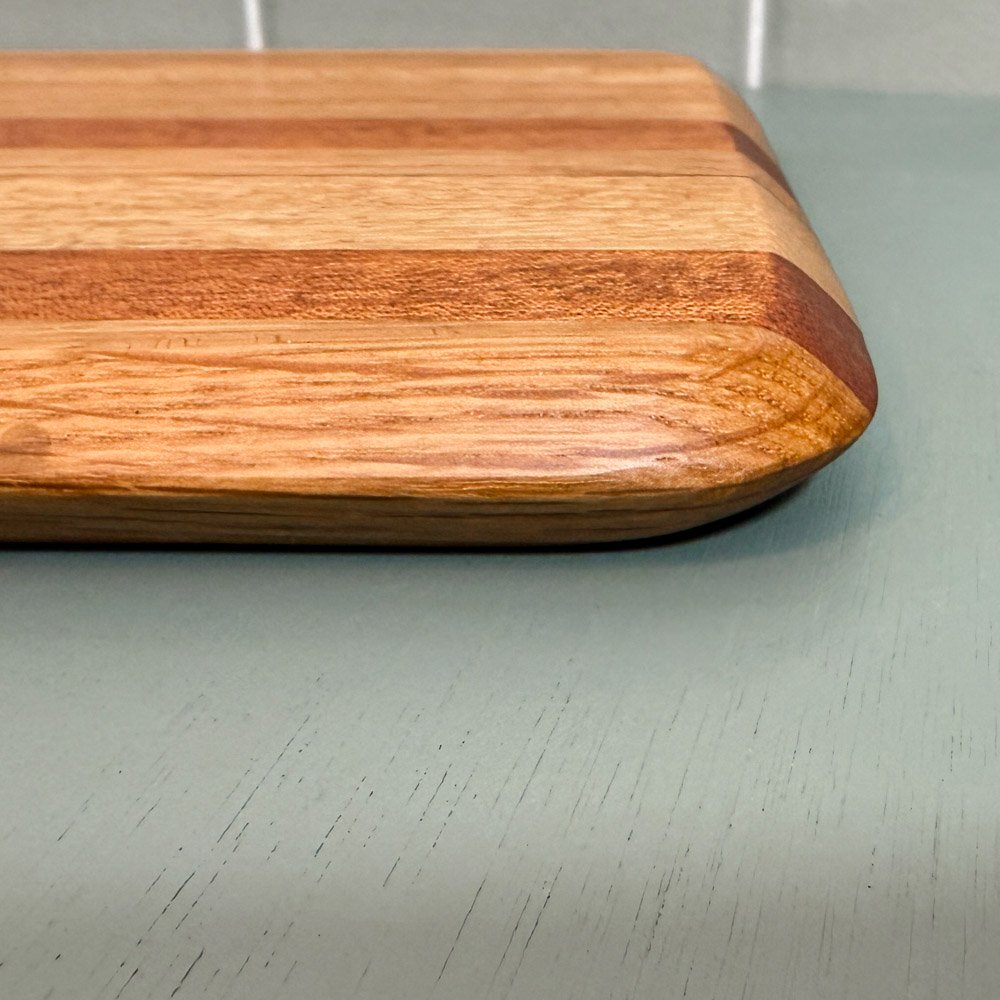 subtly striped handmade oak and mahogany chopping board made from oak and mahogany laying on a green table