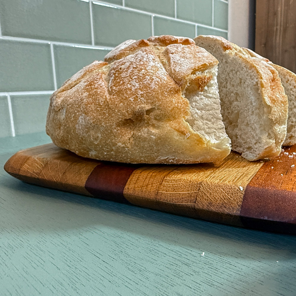 subtly striped handmade oak and mahogany chopping board made from oak and mahogany laying on a green table styled with bread with a green tiled background