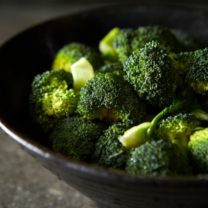 A dark bowl full of broccoli florets on a dark table to illustrate how good broccoli is for our skin health