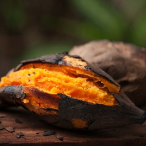 Two baked sweet potates with their jackets on. The one at the front is split open and the orange flesh of the sweet potato can be seen. There is a dark green background. This image represents the idea that carotenoids are good for healthy skin