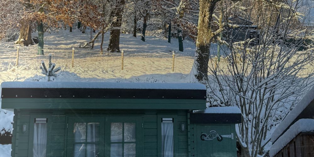 a photo of the Ola Ròs and Made in the Glen lab in the snow in Glen Urquhart. The lab is a wood cabin painted in pea green by sadolin. the curtains are closed. this is the building where Made in the glen makes soaps and ola ros makes skincare