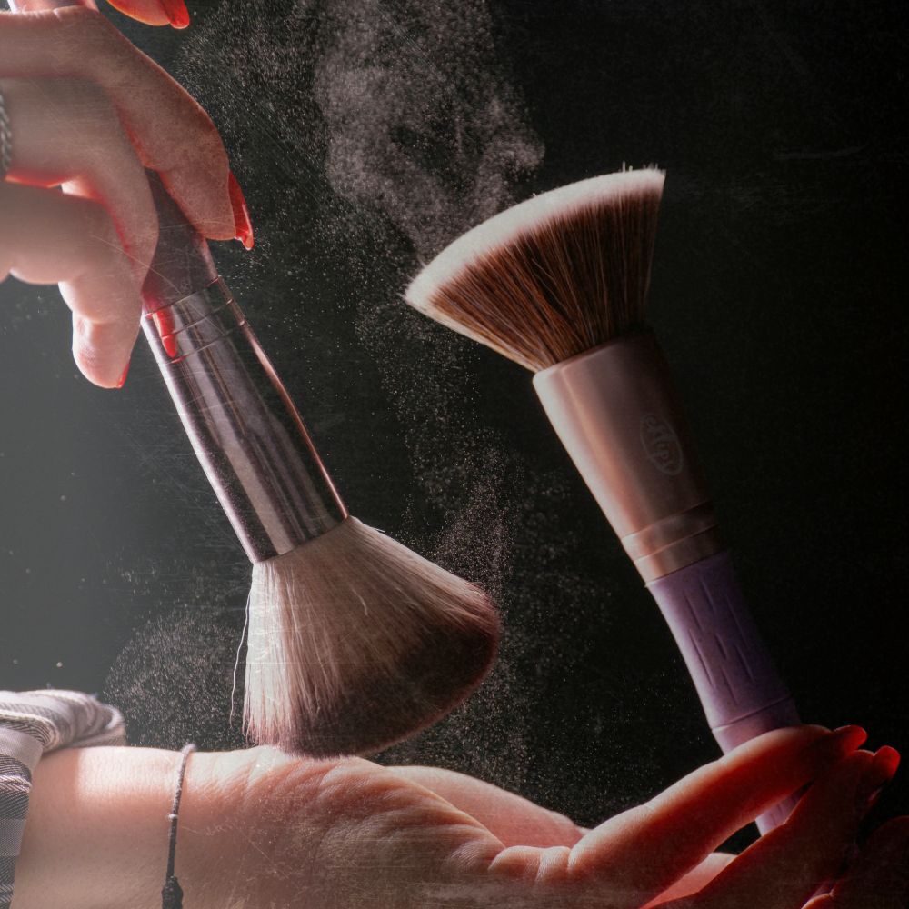 Two make up brushes and a lady's hands soft colourful makeup powders and coming off the brushes