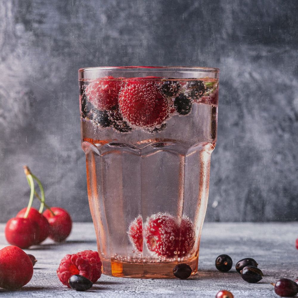 A glass of pure water with seasonal berries inside and some topples on the table next to it. a dark grey background. To depict the idea of a healthy lifestyle is part of healthy skin