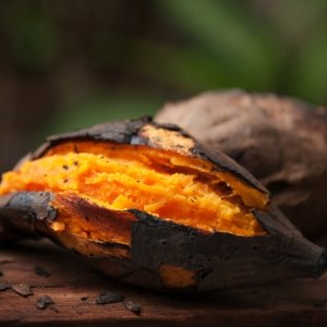 Two baked sweet potates with their jackets on. The one at the front is split open and the orange flesh of the sweet potato can be seen. There is a dark green background. This image represents the idea that carotenoids are good for healthy skin