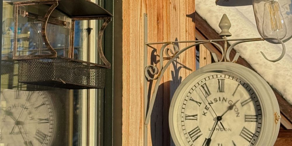 a vintage style clock on a cast iron bracket the clock is on the side of a wooden building cladded with larch the building is used as the Made in the Glen studio where