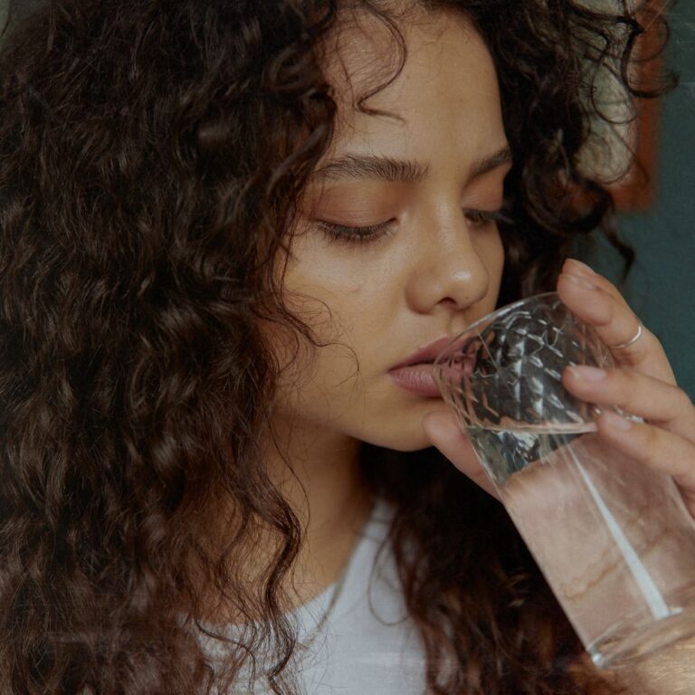 lady drinking a glass of water to keep her skin hydrated from within