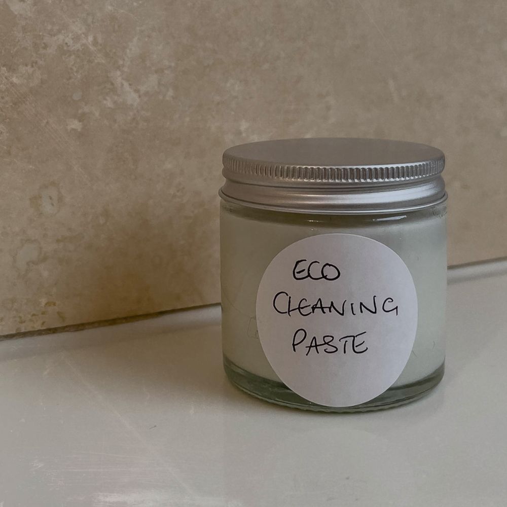 a glass jar of DIY eco cleaning paste sat on a bathtop with travertine tiles behind