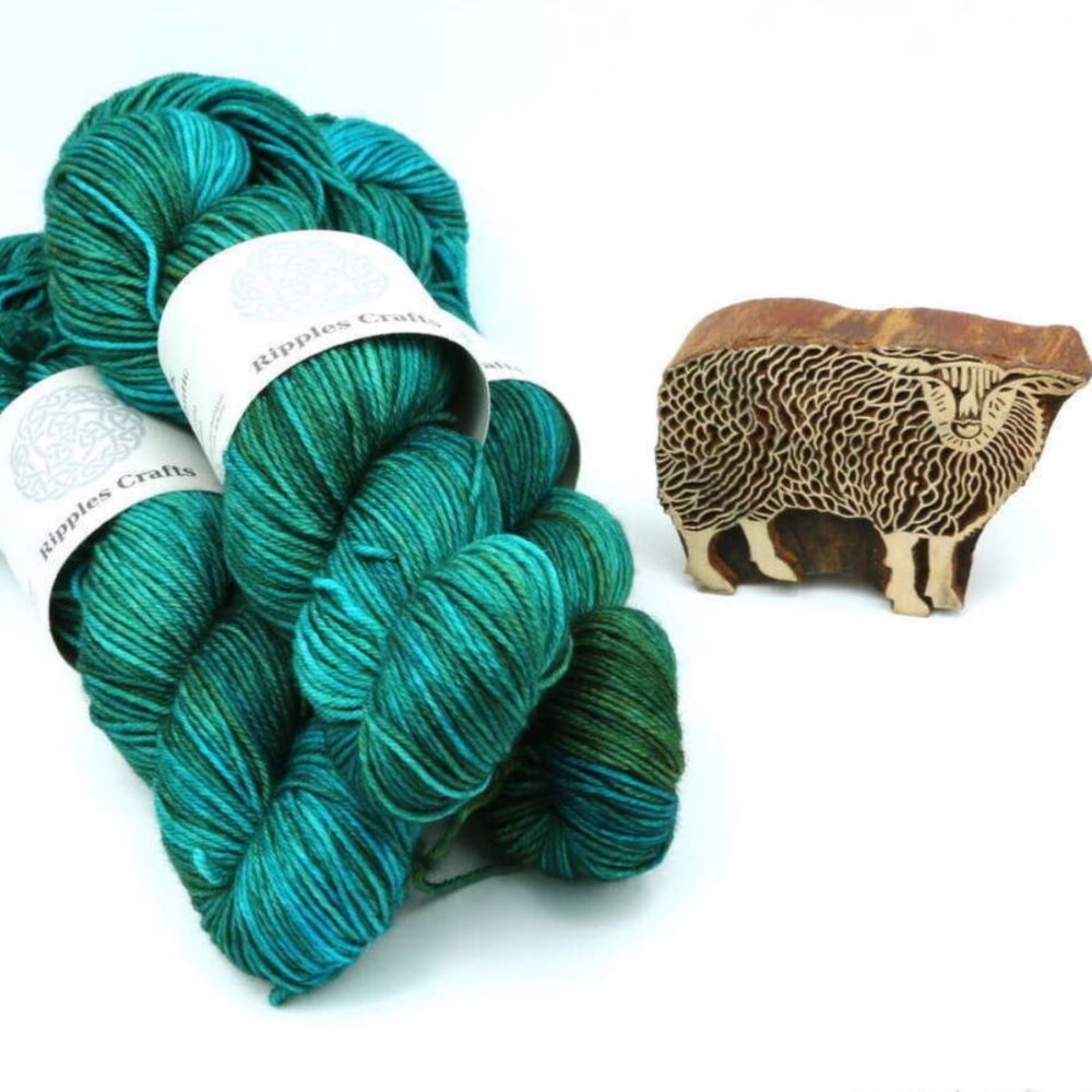 three skeins of hand dyed wool laid on a table next to a hand carved wooden sheep. the wool was hand dyed by ripples crafts