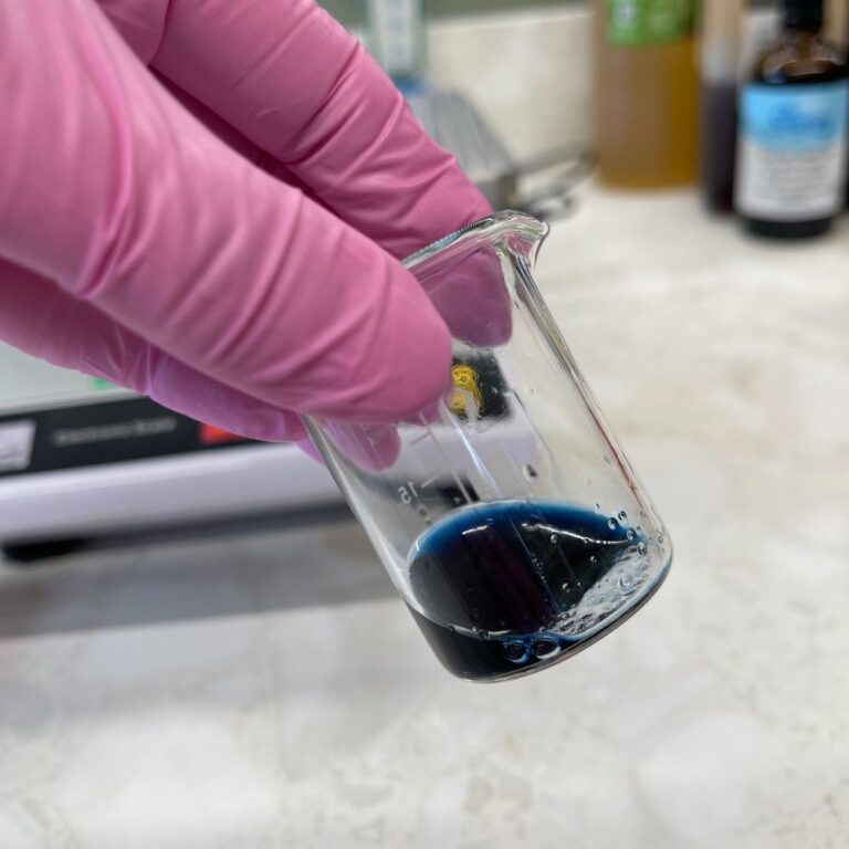 Blend of essential oils for the Ola Ros Restore Facial oil in a small lab beaker being tipped to one side by a gloved hand
