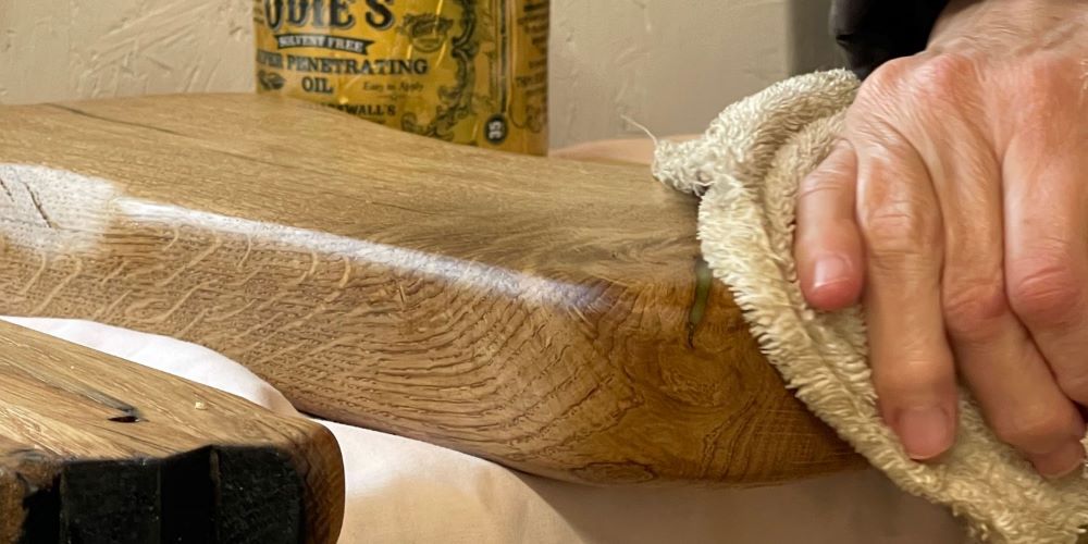 a handmade oak board being polished by hand at Made in the Glen Workshop Clean Room behind the board sits a bottle of Odie's super penetrating oil