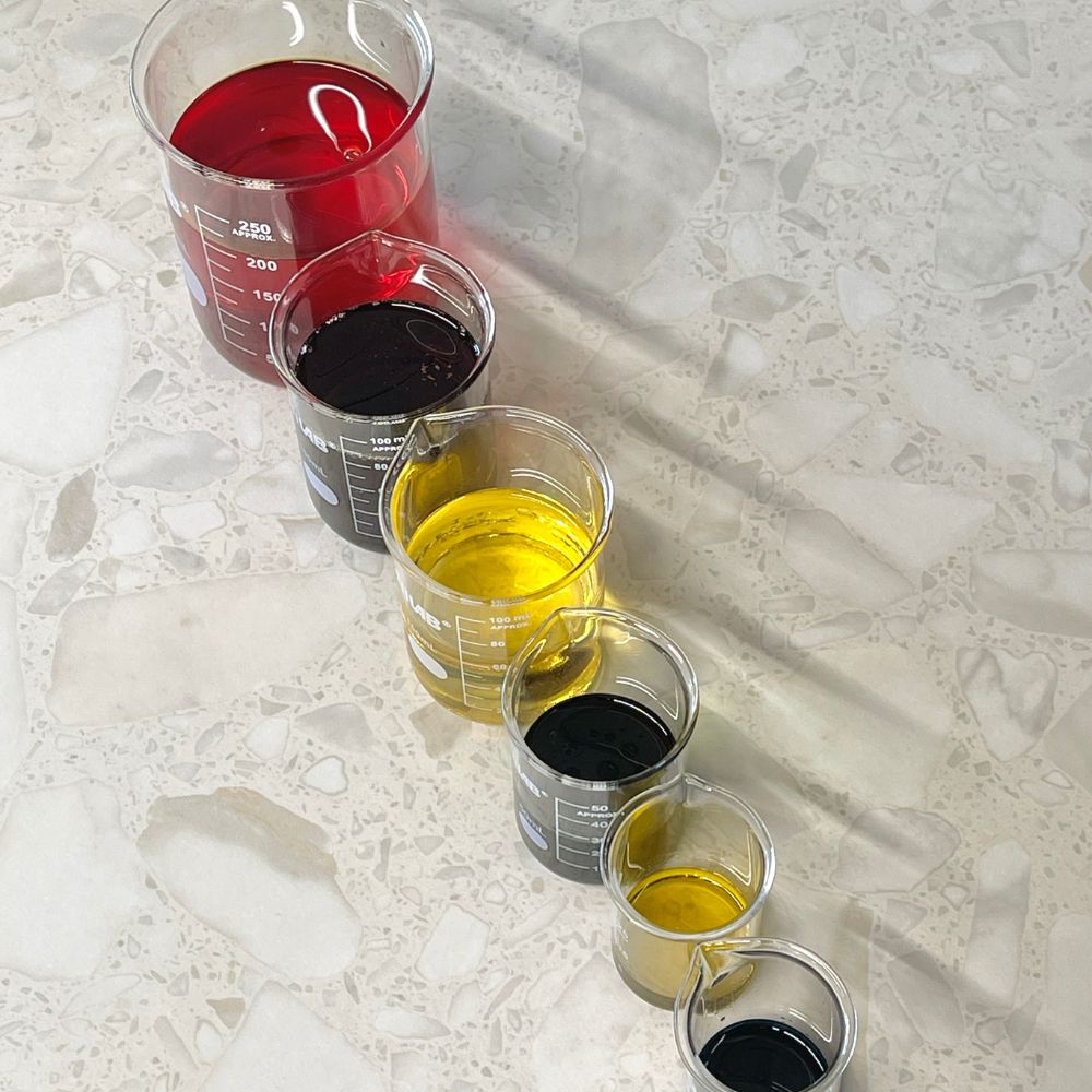a colourful selection of botanical and organic oils arranged in lab beakers in a row