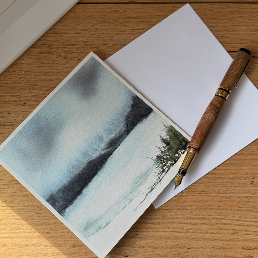 Loch Ness watercolour greeting card by Julia Anne displayed with a matching envelope, highlighting UK printing in a square 150mm format.