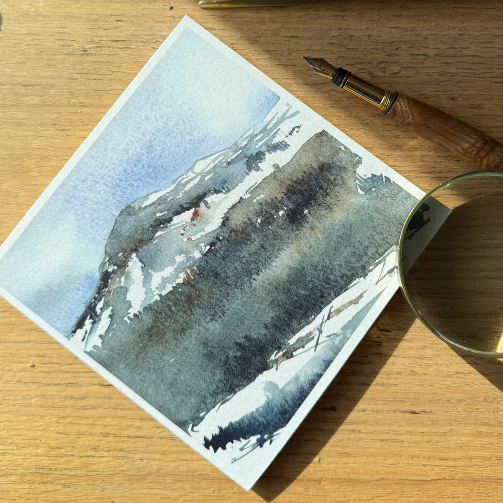 Highland Landscape watercolour greeting card by Julia Anne displayed with a matching envelope, highlighting UK printing in a square 150mm format.