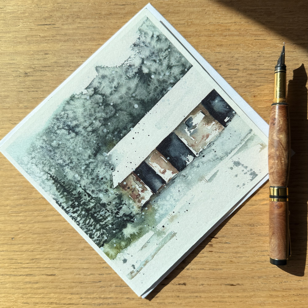 The Bothy watercolour greeting card by Julia Anne displayed with a matching envelope, highlighting UK printing in a square 150mm format.