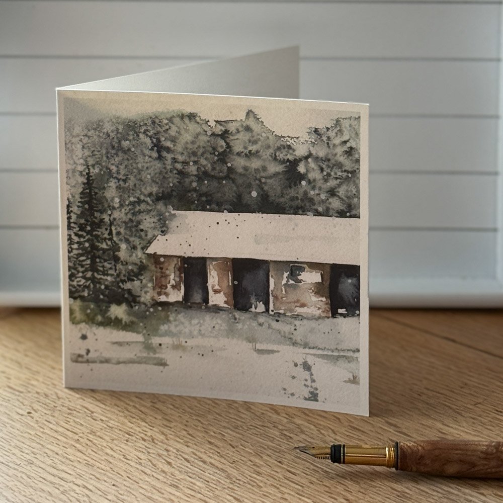 The Bothy watercolour greeting card by Julia Anne displayed with a matching envelope, highlighting UK printing in a square 150mm format.