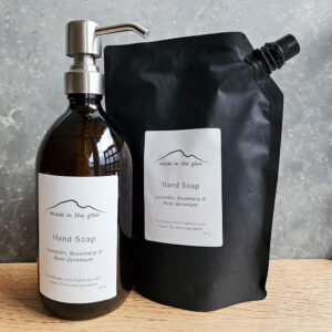 liquid hand soaps by Made in the Glen sweet orange & cinnamon Organic essential oils in an Amber glass bottle with brass metal pump filled with Made in the Glen Liquid hand soap made with organic ingredients on an oak worktop in the bathroom a black refill pouch is stood beside the bottle