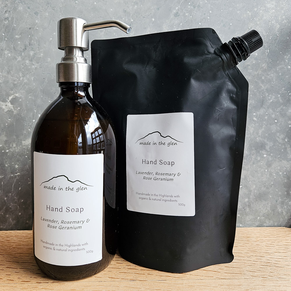 liquid hand soaps by Made in the Glen sweet orange & cinnamon Organic essential oils in an Amber glass bottle with brass metal pump filled with Made in the Glen Liquid hand soap made with organic ingredients on an oak worktop in the bathroom a black refill pouch is stood beside the bottle